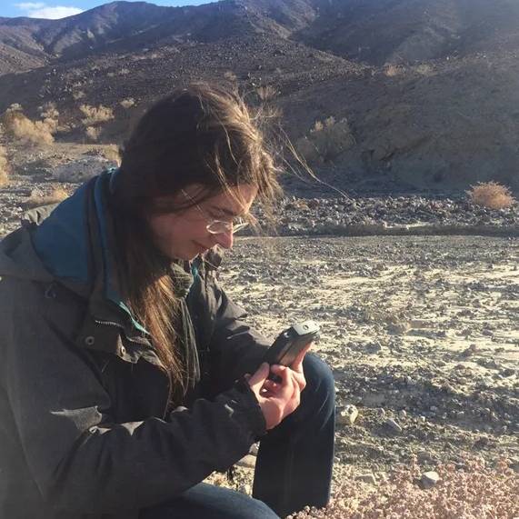 Woman kneeling in desert as she checks a small handheld device